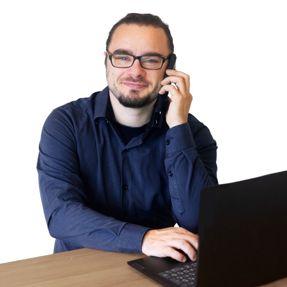 Alexander Hacker sitzt an einem Schreibtisch und hat eine Hand am Telefon
